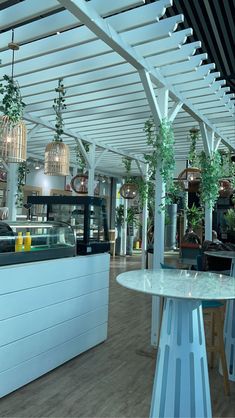 the interior of a restaurant with white tables and hanging plants on the ceiling above it