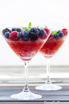 two martini glasses filled with berries and mint garnish on a wooden table top