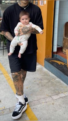 a man with tattoos holding a baby in his arms while standing next to a building