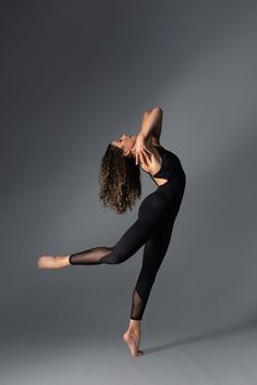 a woman in black leotard and tights is doing a dance move with her arms stretched out