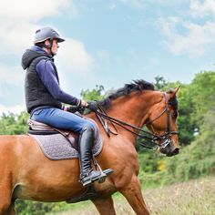 a woman riding on the back of a brown horse in a field next to trees