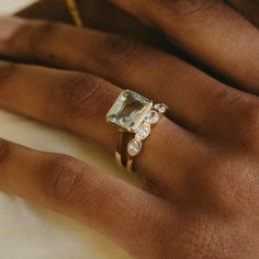 a woman's hand with a gold ring and an aquamarine colored diamond on it