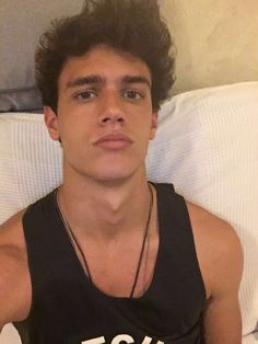 a young man wearing a tank top sitting on a bed