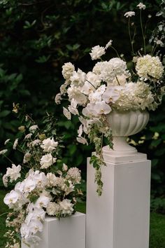 three white vases with flowers in them are sitting on pedestals near each other