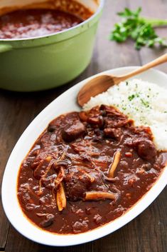 a white plate topped with meat and gravy next to a bowl of rice