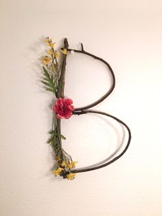 the letter b made out of branches and flowers is hanging on the wall next to a white wall