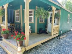 a small green house with potted plants on the porch