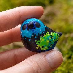 a hand holding a small blue and green bird ornament in it's palm