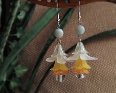 a pair of earrings with flowers hanging from them on a tree branch in front of a plant