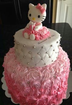 a hello kitty cake with pink ruffles and pearls on the bottom, sitting on top of a black table