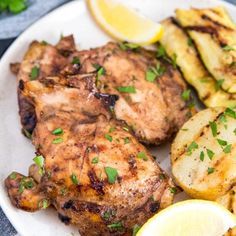 a white plate topped with chicken, potatoes and lemon wedges