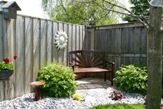 a wooden bench sitting in the middle of a garden next to a tree and fence