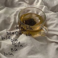 a glass cup filled with tea sitting on top of a white blanket covered in writing