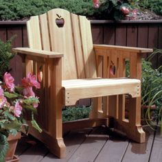 a wooden chair sitting on top of a lush green field next to flowers and trees