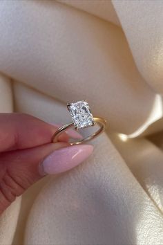 a woman's hand holding a diamond ring on top of a white cloth background