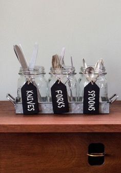 four mason jars with forks and spoons in them sitting on a wooden table next to a drawer