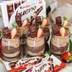 desserts with chocolate and strawberries in small jars on a table next to some candy bars