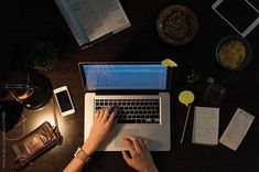 a person using a laptop computer on top of a wooden table next to other items