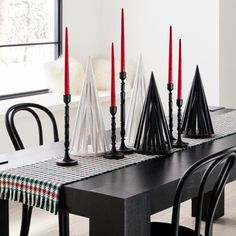 a dining room table with black chairs and red candles on top of the placemats