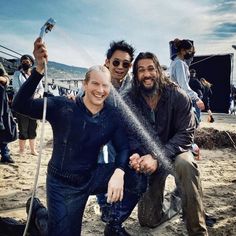 three men are standing in the sand with water spraying from their hands and smiling at the camera