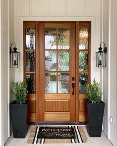 a welcome mat is on the front door of a house with two planters and potted plants