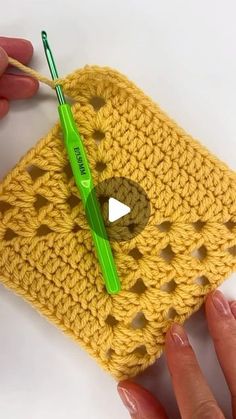 a crochet square being worked on by someone using a green knitting needle to hold it