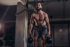 a shirtless man holding two kettles in a gym