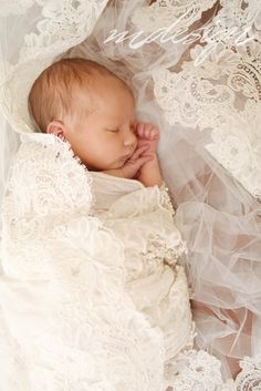 a newborn baby wrapped in a white lacy blanket with her hands under her chin and head