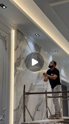 a man standing on a scaffold in front of a white marble wall and ceiling