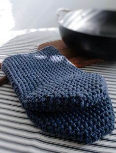 a blue knitted dish cloth sitting on top of a wooden spatula next to a black skillet