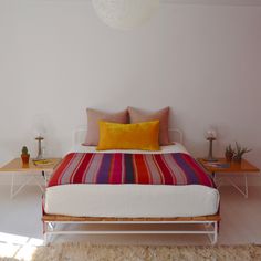 a bed sitting on top of a white floor next to a table with two lamps