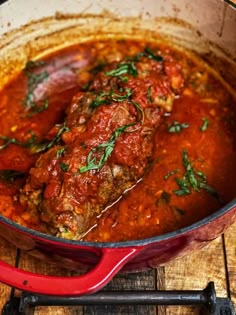 a red pot filled with meat covered in marinara sauce and garnished with parsley