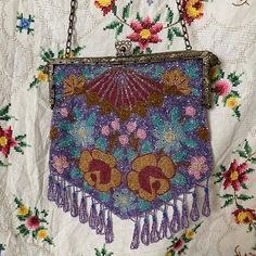 an embroidered purse hanging from a chain on top of a tablecloth covered with flowers