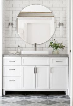 a white bathroom vanity with a round mirror above it and a plant on the counter