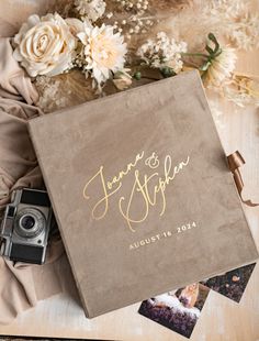 a wedding album with gold lettering on it and flowers next to the album is an old camera