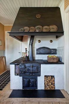 an old fashioned stove is in the middle of a room with wood stacked on the floor