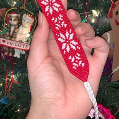 a hand holding a red crocheted christmas tie in front of a christmas tree