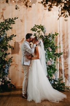 a bride and groom kissing in front of a floral backdrop at the end of their wedding day