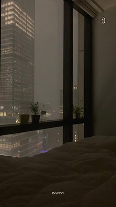 a bed sitting next to a window in a bedroom under a sky scraper at night