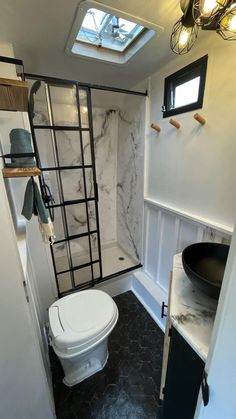 a white toilet sitting next to a shower in a bathroom under a skylight on top of a tiled floor