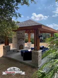 an outdoor living area with stone fireplace and seating under a wooden gazebo surrounded by palm trees