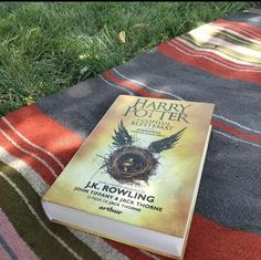 a harry potter book sitting on top of a blanket next to a green grass covered field