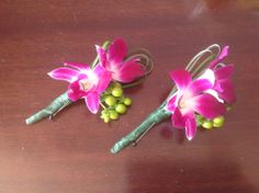 two pink flowers are sitting on a table with green leaves and buds attached to the stems