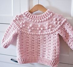 a pink knitted sweater hanging on a white door frame with a wooden hanger