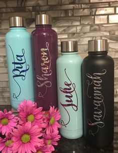 three personalized water bottles sitting next to a pink flower on a counter top with a brick wall in the background