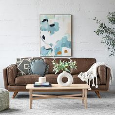 a living room with a brown couch, coffee table and potted plant in the corner