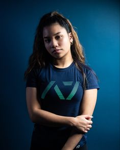 a woman with her arms crossed standing in front of a blue background wearing a t - shirt