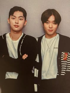 two young men standing next to each other in front of a wall with their arms crossed