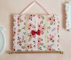 a pink flowered wall hanging with a red bow on it's tie bar