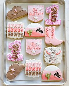 decorated cookies in the shape of cowboy hats and boots on a cookie sheet with pink frosting